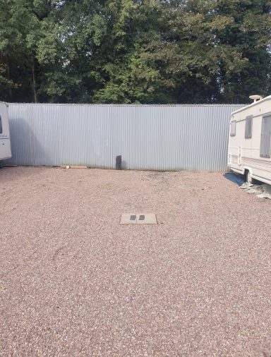 Gravel area between two caravans with a grey wall in the background.