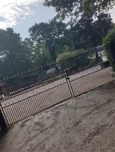 Rustic gate leading into a green, tree-lined entrance area.